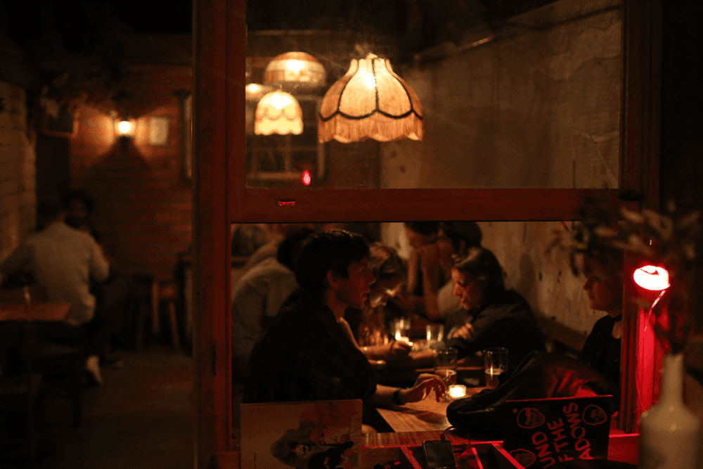 Image looking out to the courtyard. Records are playing on the turntables. People drinking cocktails on tables underneath old lampshades.